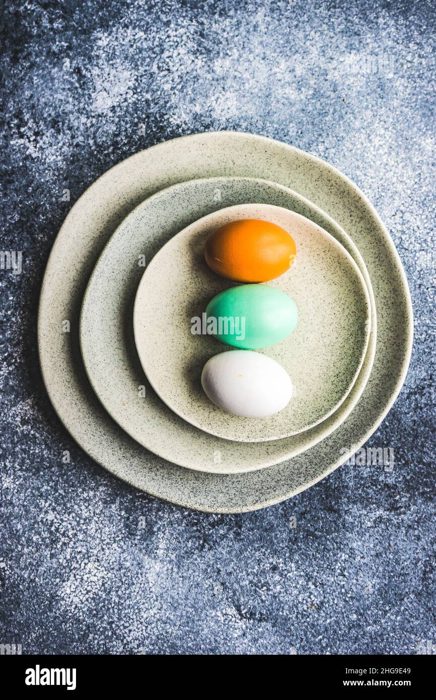 Overhead view of three painted Easter eggs on ceramic plates Stock Photo