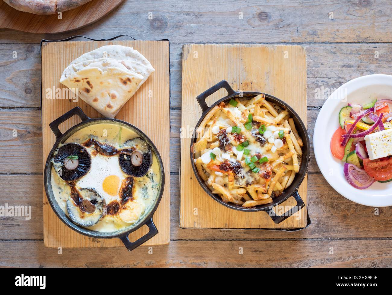 Delicious artisan cast iron skillet cheesy egg and mushroom sizzler and loaded fries, shot from above Stock Photo