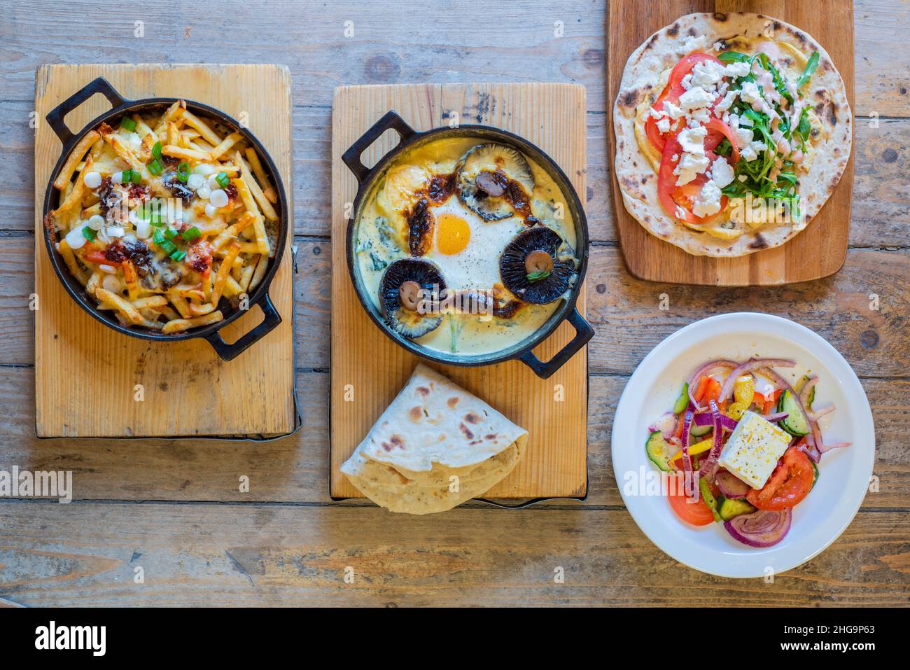 Delicious artisan cast iron skillet cheesy egg and mushroom sizzler and loaded fries, chicken wrap and feta salad shot from above Stock Photo