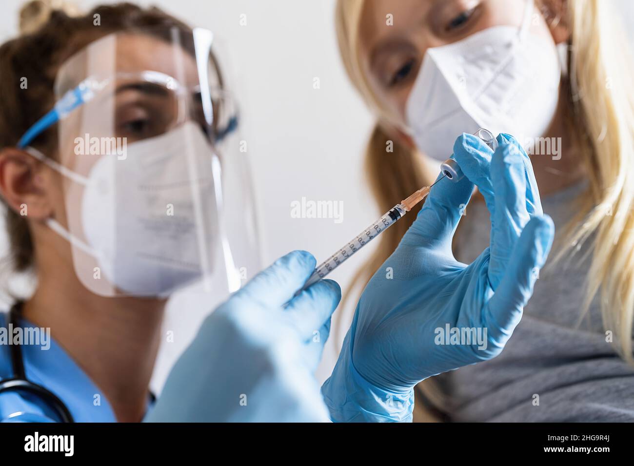 blonde child girl looking at the Syringe with vaccine for covid-19 coronavirus, flu, dangerous infectious from a healthcare worker. While being vaccin Stock Photo