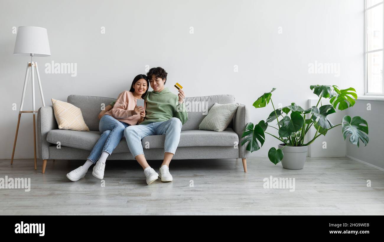 Shopping online. Young Asian couple making purchases on mobile phone, holding credit card, using web banking service Stock Photo