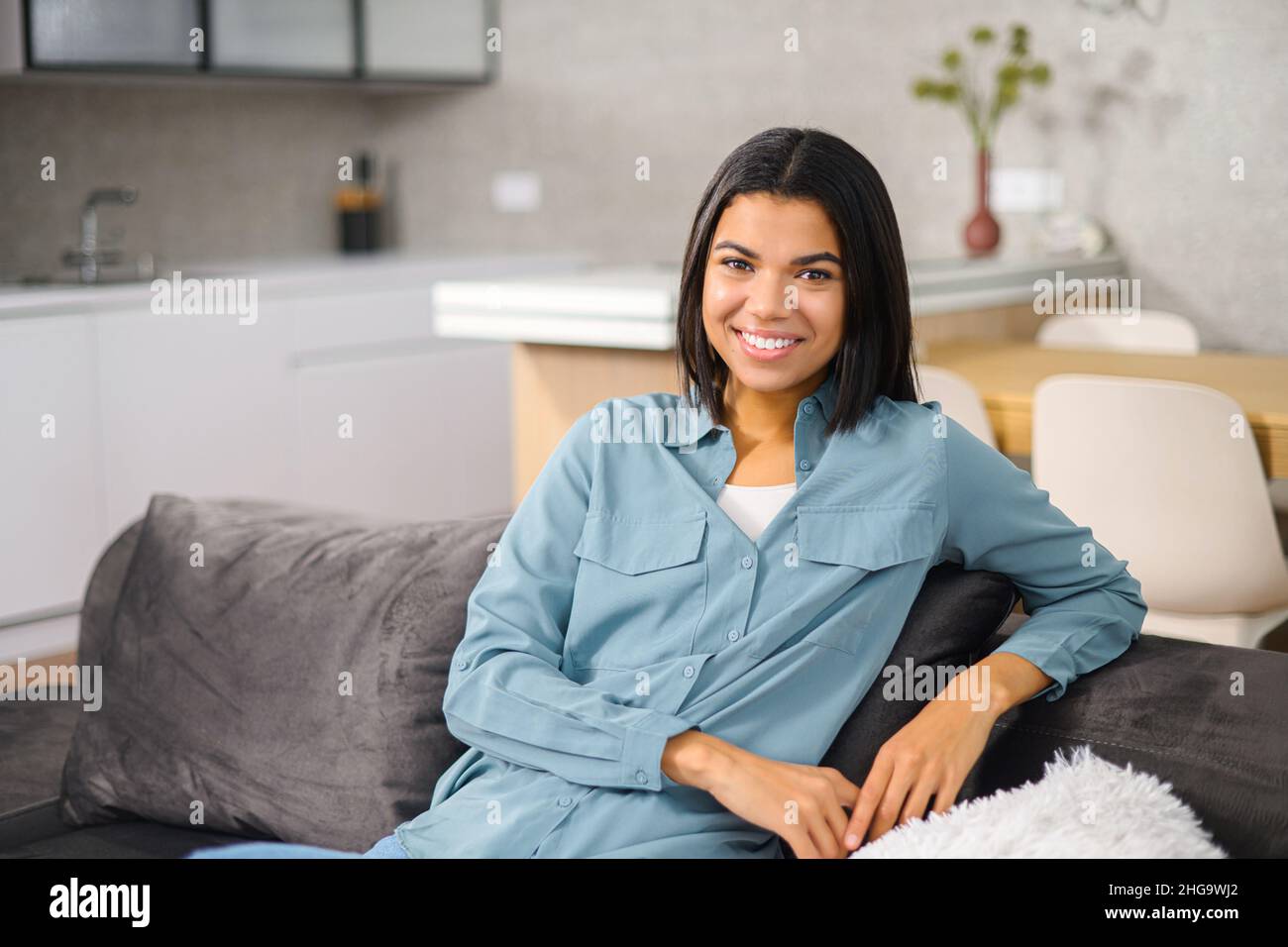 Carefree multiracial woman resting on the comfortable couch at home, while feeling happy. Charming woman looking at camera and smiling while resting at home Stock Photo
