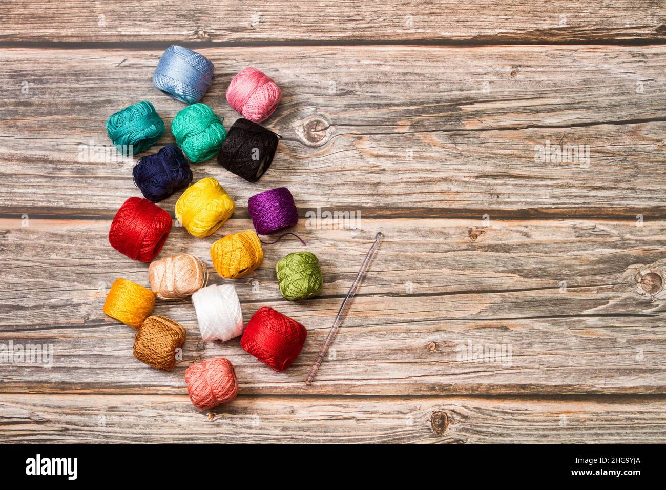 Colored yarn spools and a crochet needle on a wooden background with copy space Stock Photo