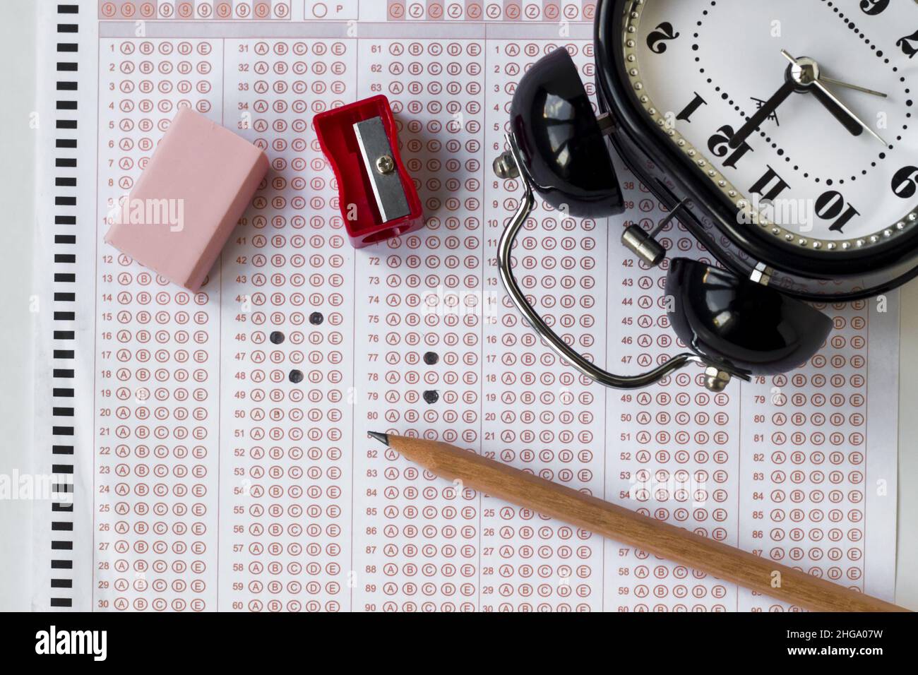 Alarm clock,wooden pencil and rubber on filled exam sheet,conceptual image of education qualifying test exam. Stock Photo