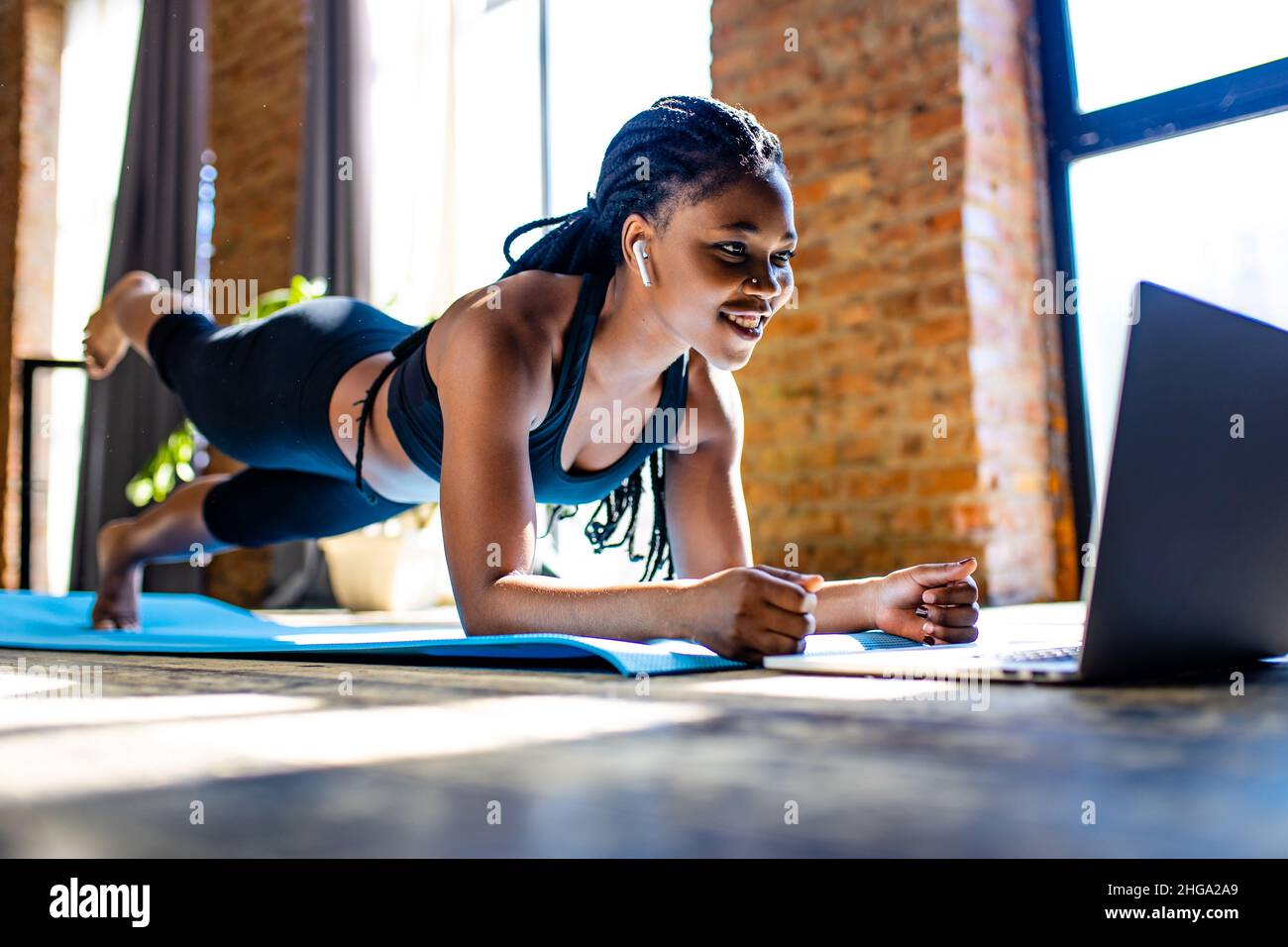 mixed race healthy woman in black sporty suit during her fitness workout at home against the background of panoramic windows sunlight Stock Photo
