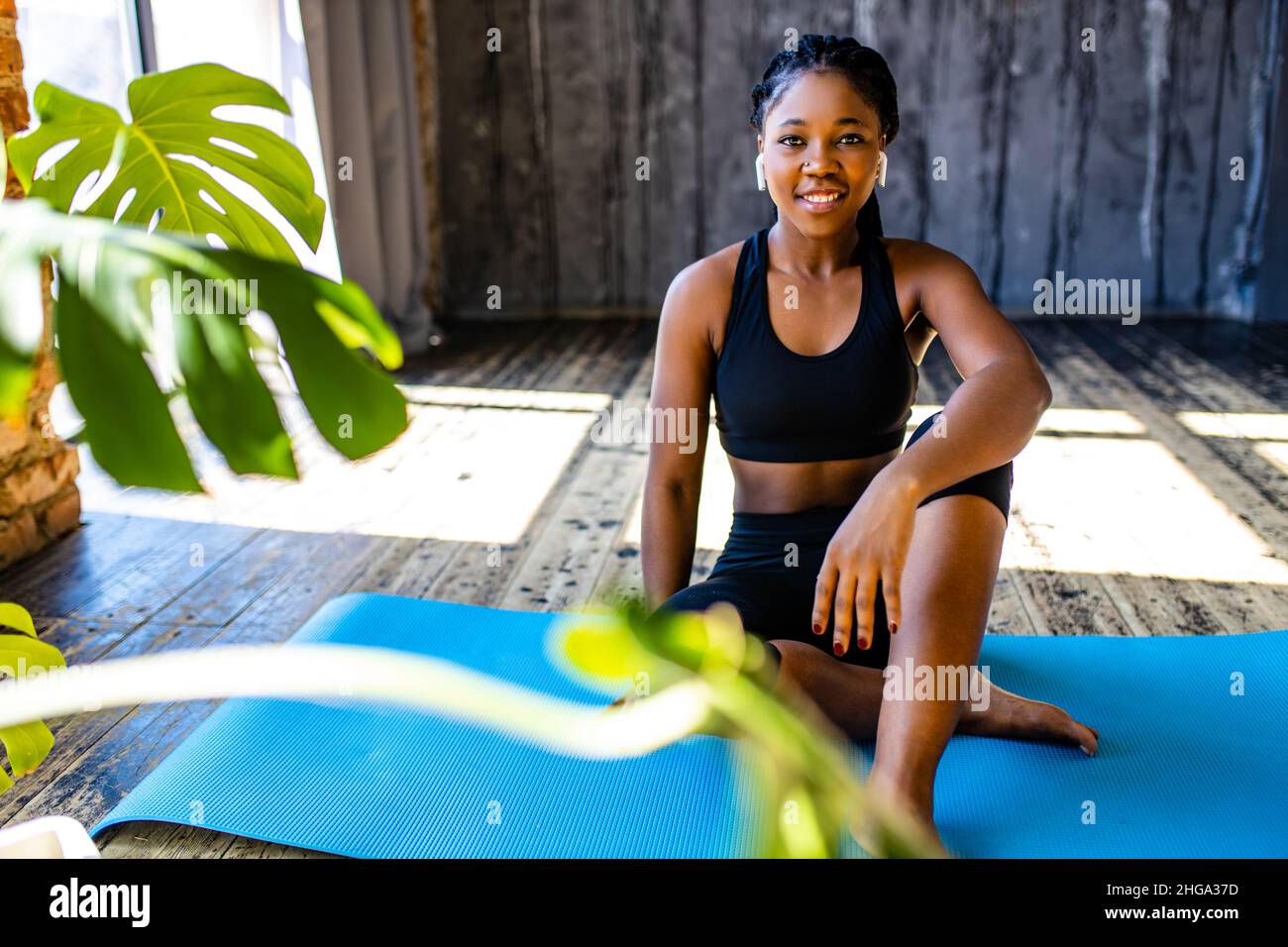 mixed race healthy woman in black sporty suit during her fitness workout at home against the background of panoramic windows sunlight Stock Photo