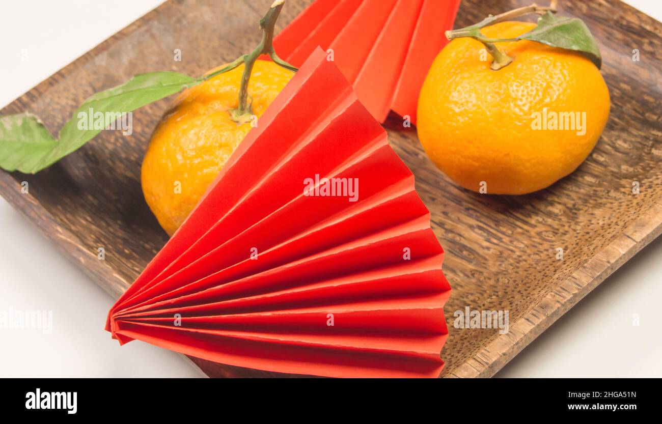 Chinese New Year, composition with tangerines, funny origami made of red paper on a dark wooden plate on a white background. Stock Photo