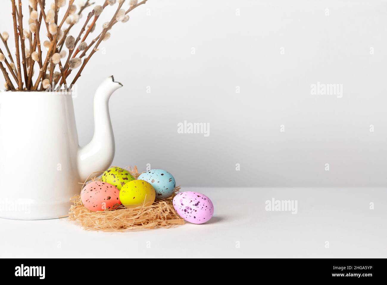 Colorful Easter eggs on a nest with pussy willow twigs in a jug, white background, copy space for Happy Easter text. Stock Photo