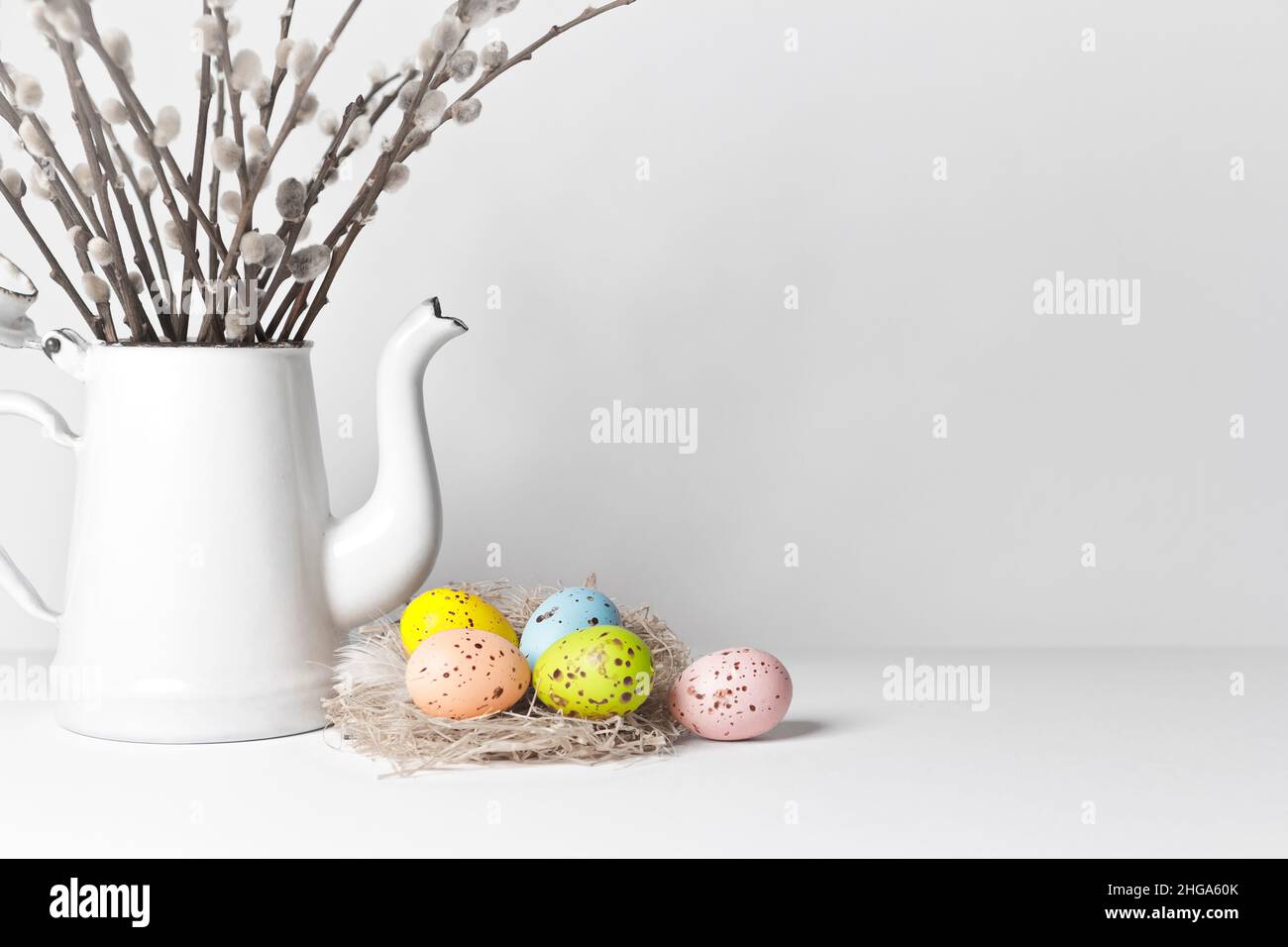 Easter eggs in soft colors on a nest with pussy willow twigs in a jug, white background, copy space for Happy Easter text. Stock Photo