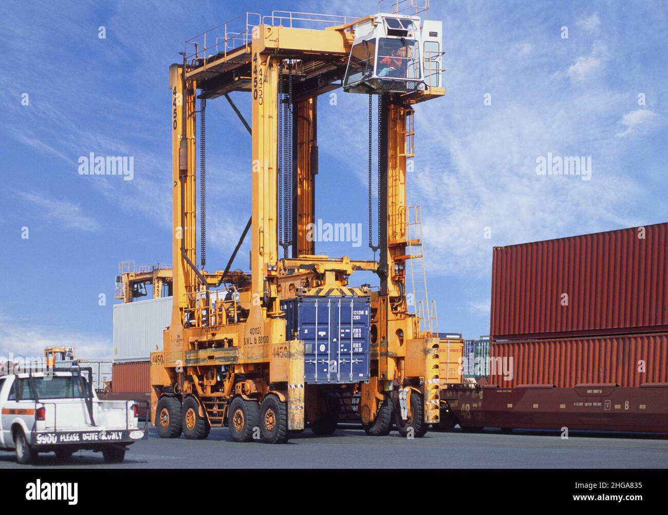 Straddle carrier with container at port pier. Loading freight cargo. Shipping. Dockside industrial seaport. Moving containers shipment on dock. USA Stock Photo