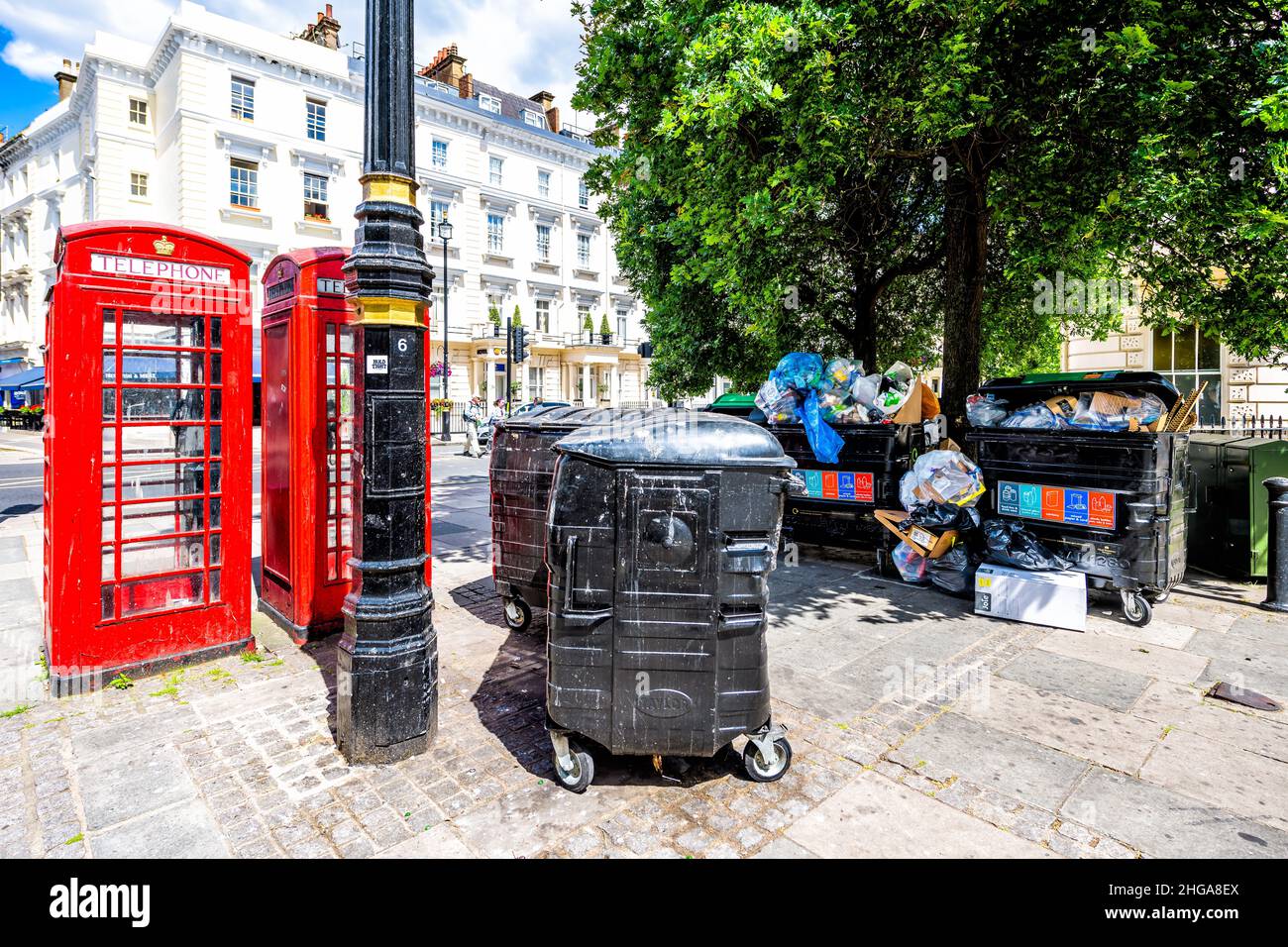 London, UK - June 21, 2018: Street sidewalk road in Pimlico Westminster district area with red telephone booth and trash dumpster with dirty garbage r Stock Photo