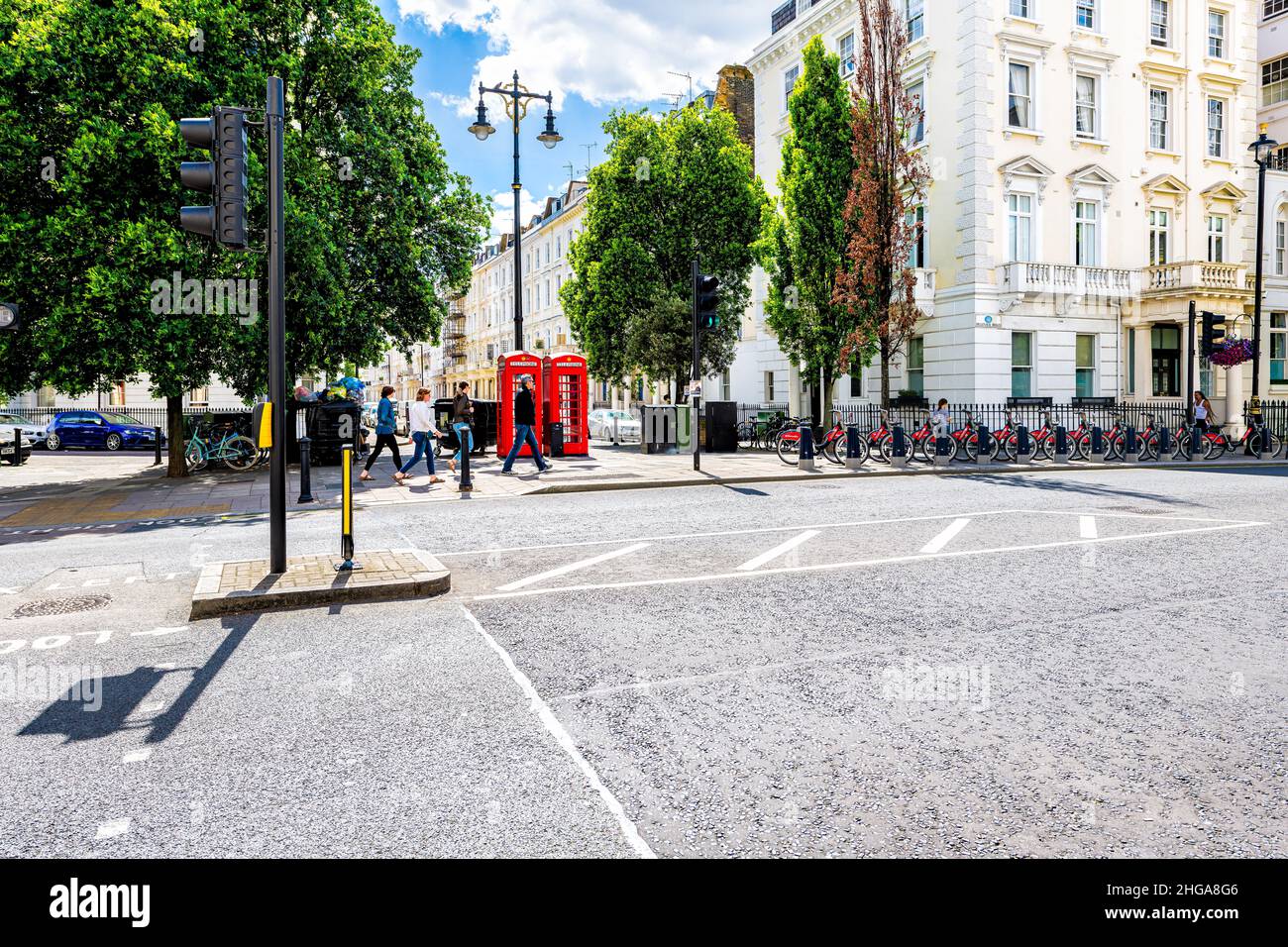 London, UK - June 21, 2018: Pimlico district neighborhood area street road with red telephone booths boxes and bikeshare rack of bicycles bikes by his Stock Photo