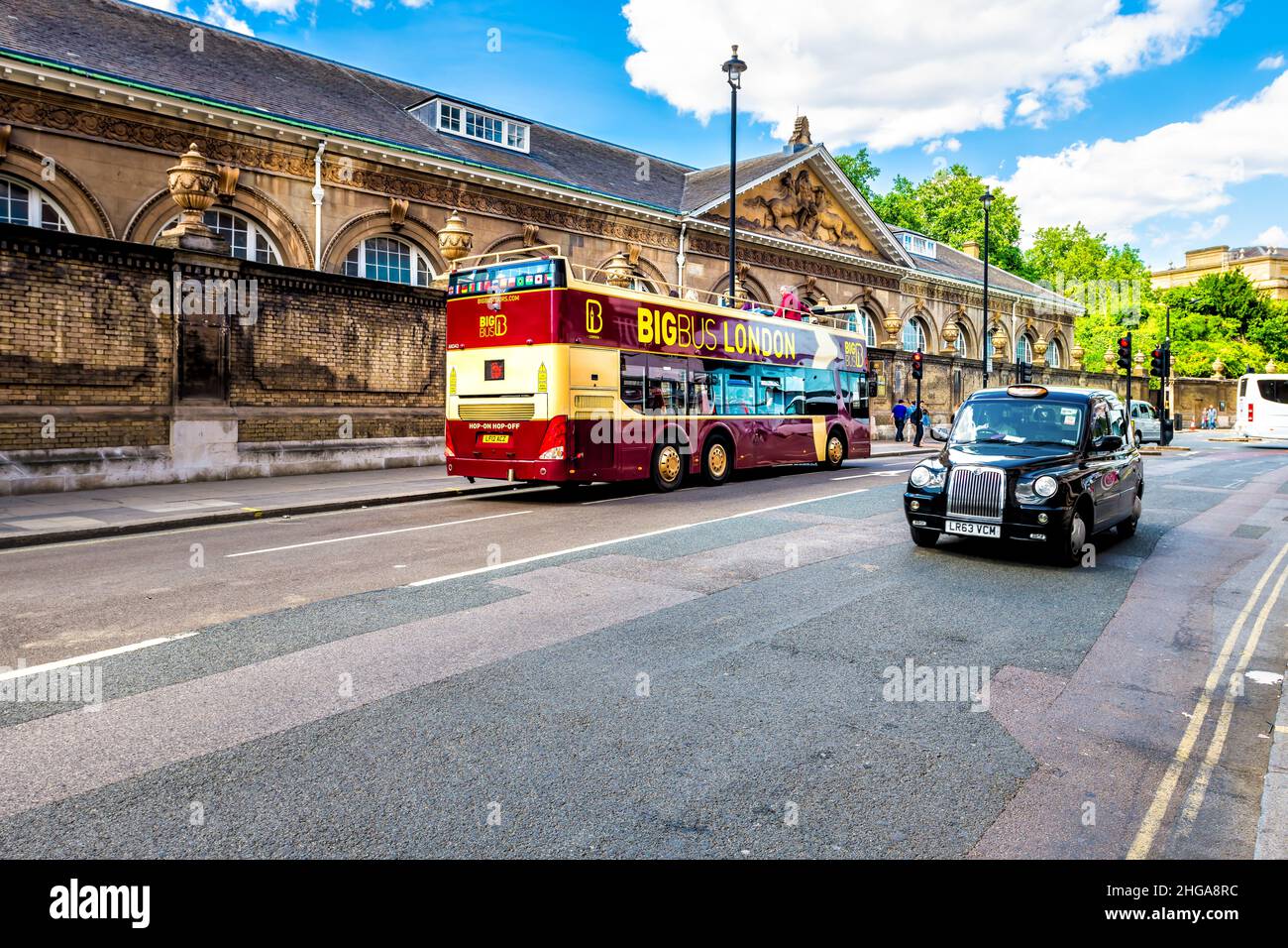 London, UK - June 21, 2018: Cars and BigBus big tour bus double decker on road by Buckingham palace with black taxi cab and Royal Mews building Stock Photo