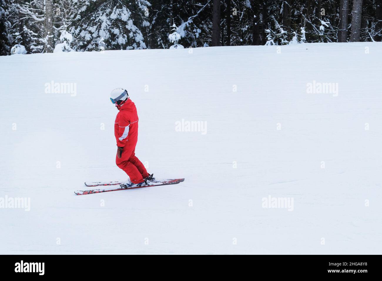 Snowboarder in red ski suit rises on lift up  mountain slope. Ski sports in winter. Vacation in mountains in ski resort. Stock Photo