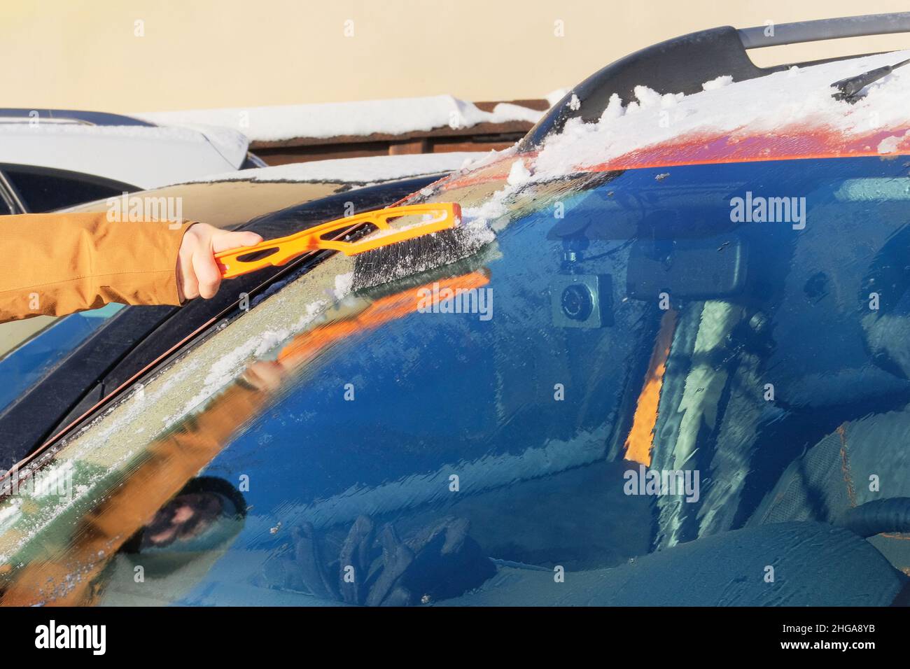 Man clears orange car from snow. Windshield of car. Brush in mans hand. Winter, snow, vehicle. Stock Photo
