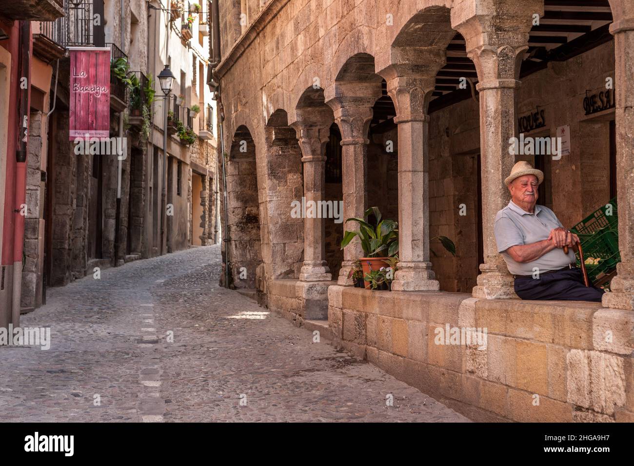 An old man with a straw hat and walking stick taking a nap under the arches in an old Spanish street Besalu Spain Stock Photo