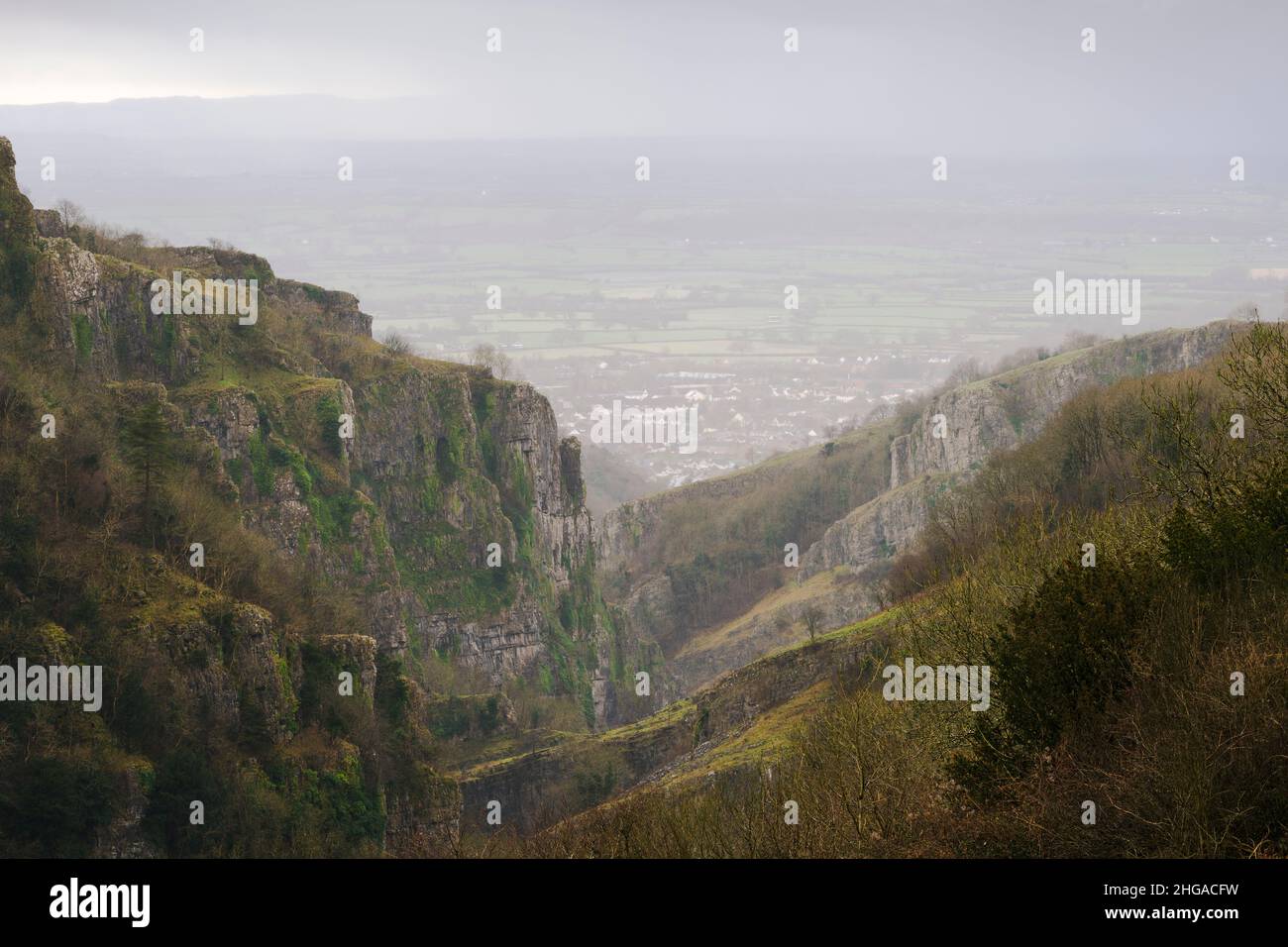 The limestone cliffs of Cheddar Gorge in the Mendip Hills with the village of Cheddar and Somerset Levels beyond during a rainstorm in winter, Somerset, England. Stock Photo