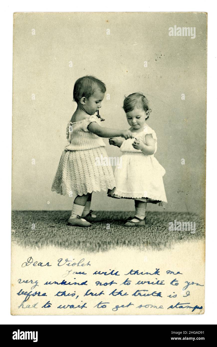 Edwardian greetings postcard depicting two cute children / toddlers holding hands, the baby on the left is probably a boy wearing a dress as was normal at this time, posted in 1904 from the U.K. Stock Photo