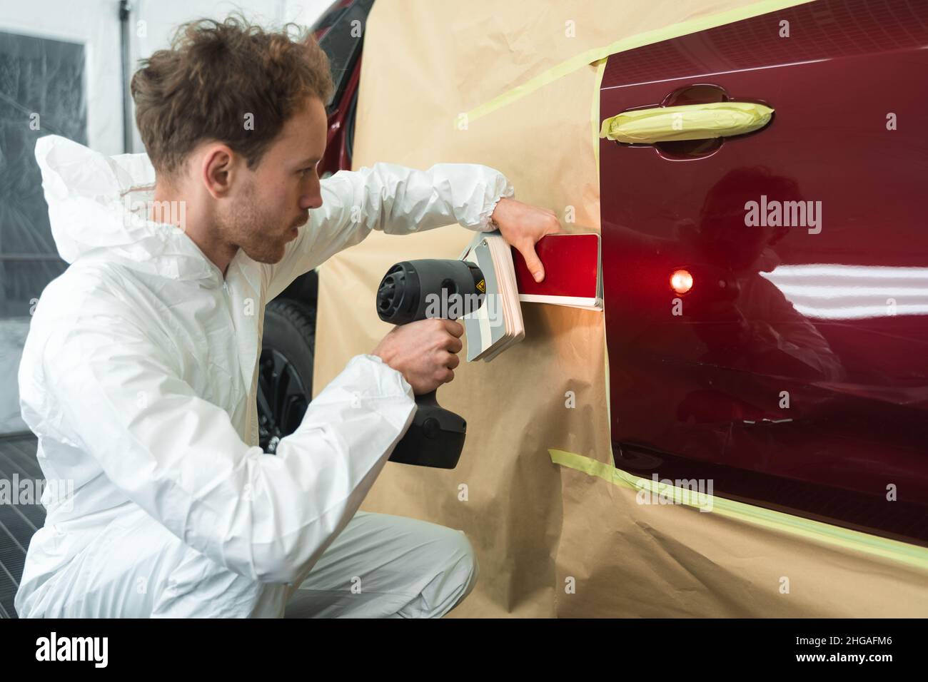Male colorist compares color sample to car paint using special lamp