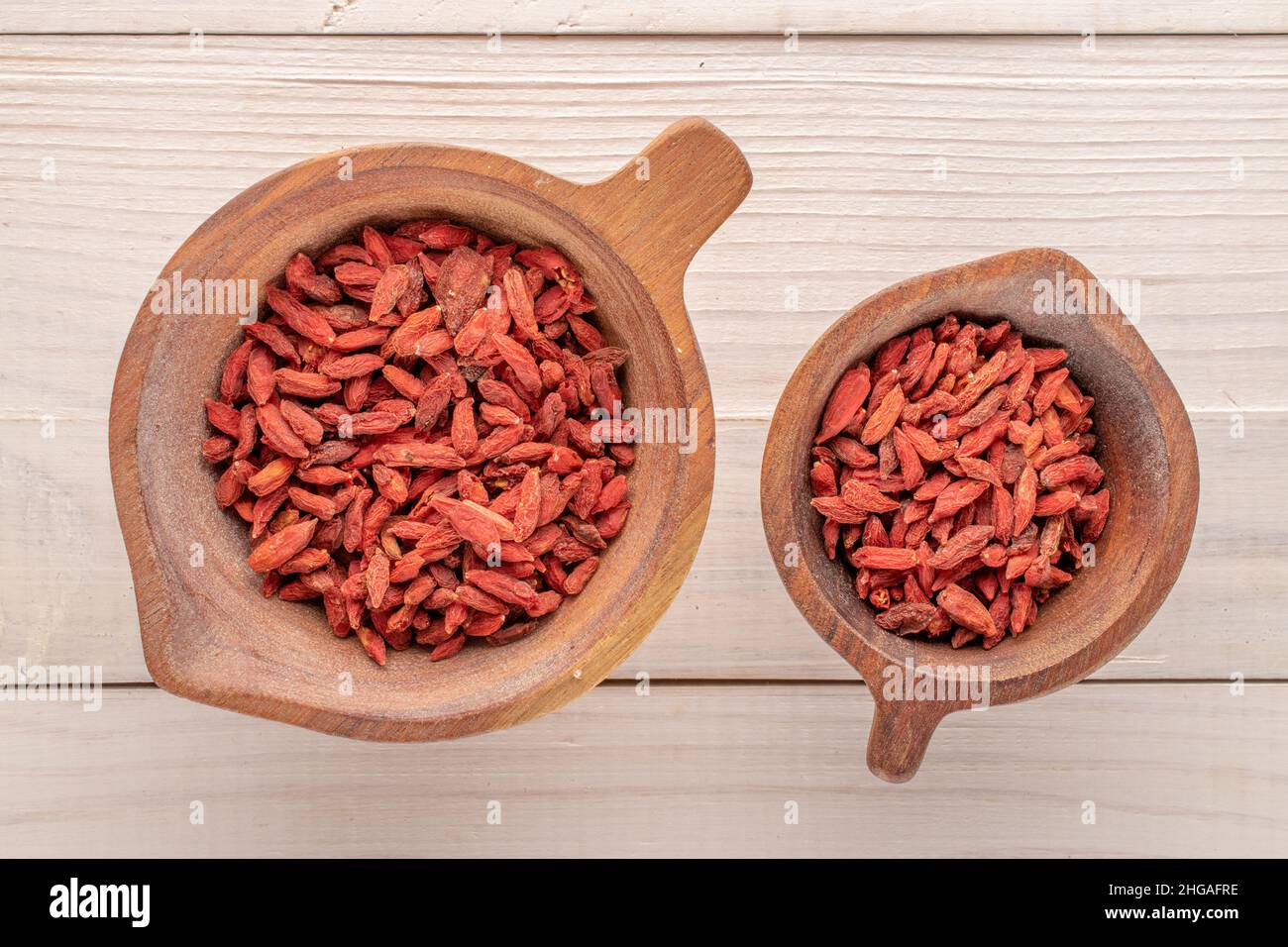 Dried organic goji berries in two wooden cups on a wooden table, macro, top view. Stock Photo