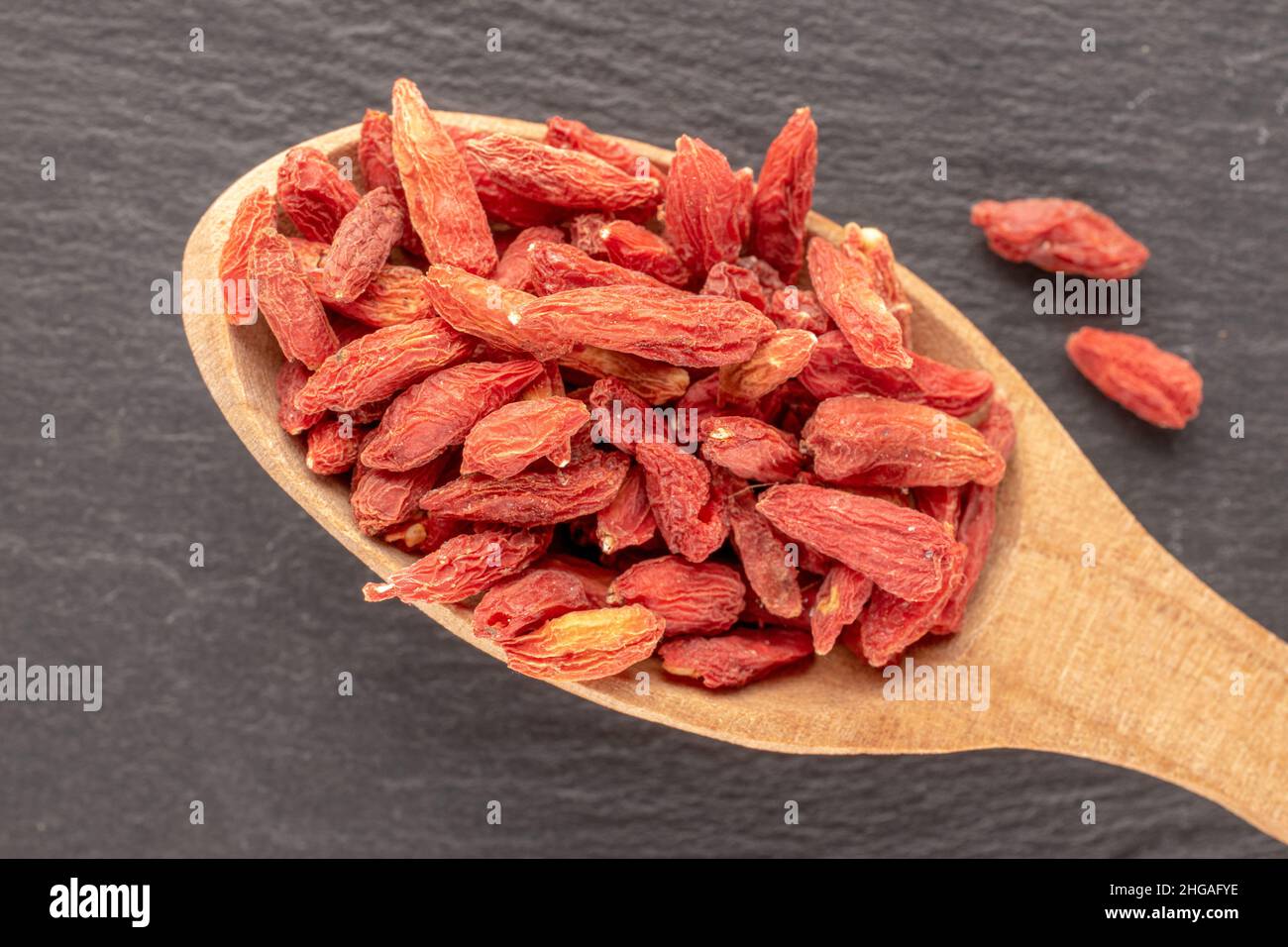 Dried organic goji berries with a wooden spoon on a slate stone, macro, top view. Stock Photo
