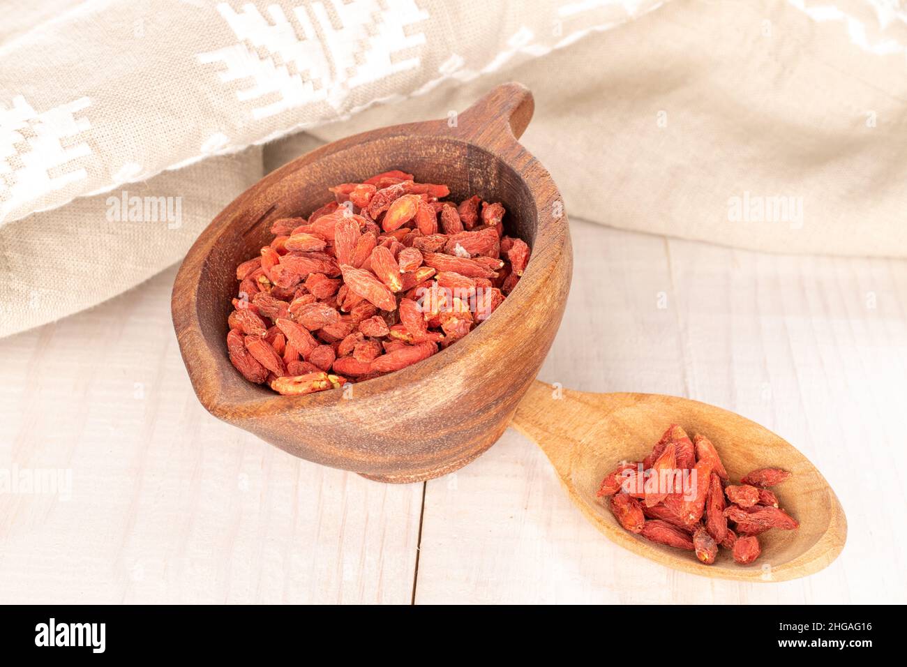 Dried goji berries in a wooden cup and with a wooden spoon on a wooden table, macro. Stock Photo