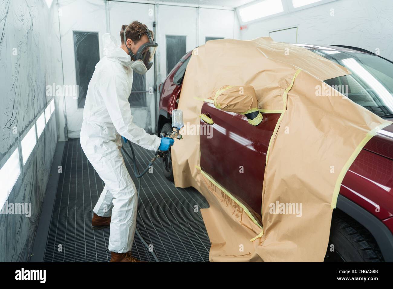 Auto painter in a protective suit and mask sprays a degreaser or other