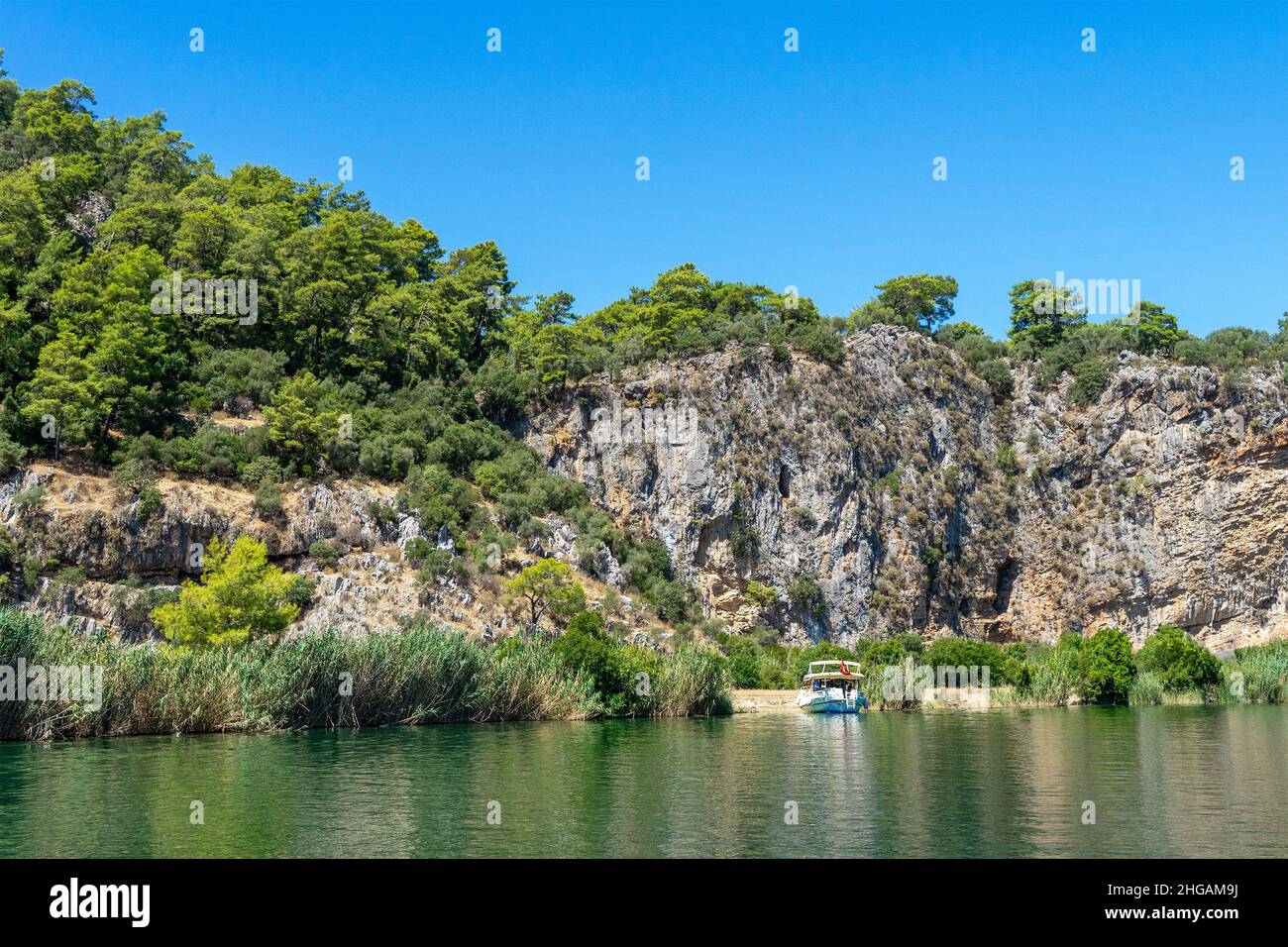 Tourist pleasure boat on the Dalyan River, next to the rocks, which contain the Lycian tombs, in Mugla Province, Turkey Stock Photo