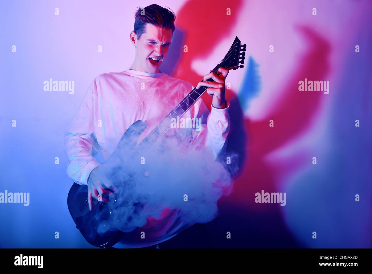 Portrait of young man artist singing, screaming, playing electric guitar Hobby, music concept. Rock Star neon light photo. Stock Photo