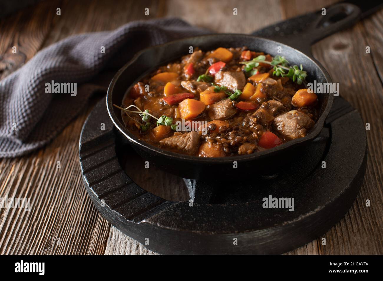 High protein fitness meal with a spicy chicken stew cooked with vegetables and lentils. Served in a rustic cast iron pan with weight plate Stock Photo