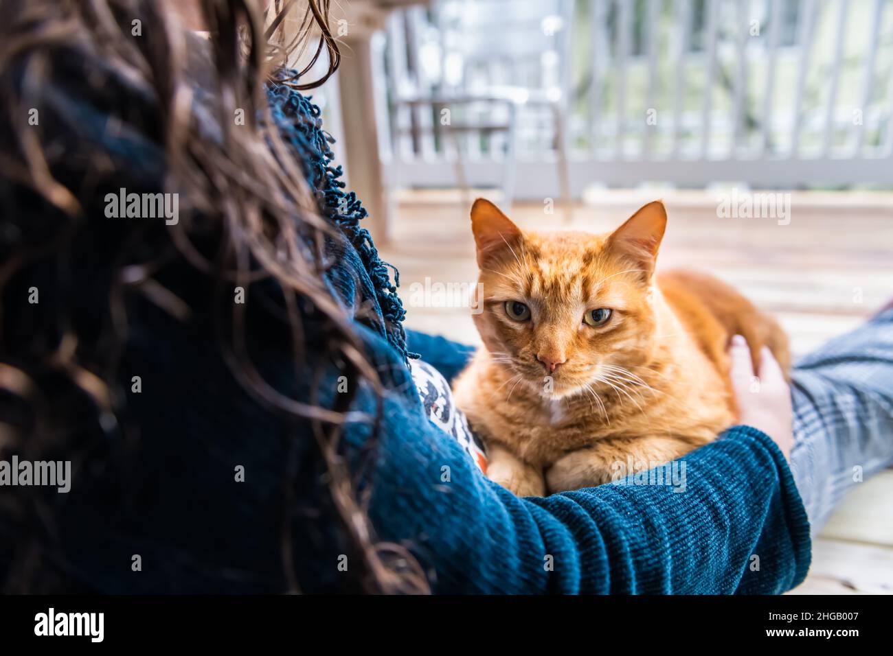 Woman sitting on floor holding lap cat in arms caressing petting stroking orange ginger kitty outside at home house balcony porch patio Stock Photo