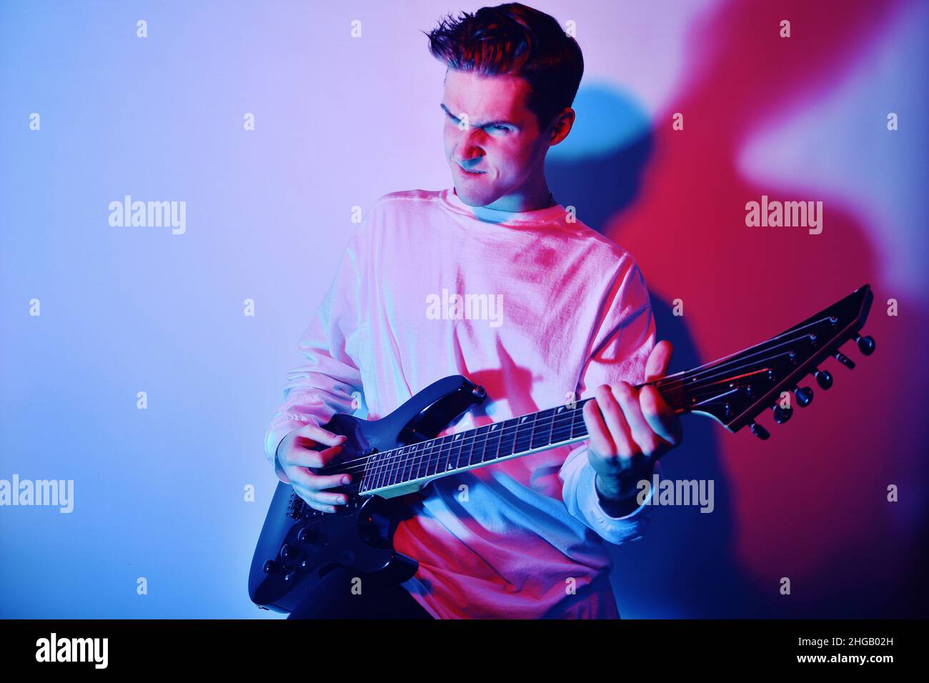 A man plays the electric guitar in neon light, red blue light. Hobbies, music, club. A man enjoys playing the guitar, screaming, vivid emotions. Stock Photo