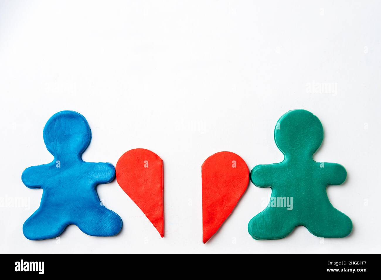 Little men made of blue and green plasticine hold in their hands halves of a red plasticine heart on a white background, copy space. Broken heart conc Stock Photo
