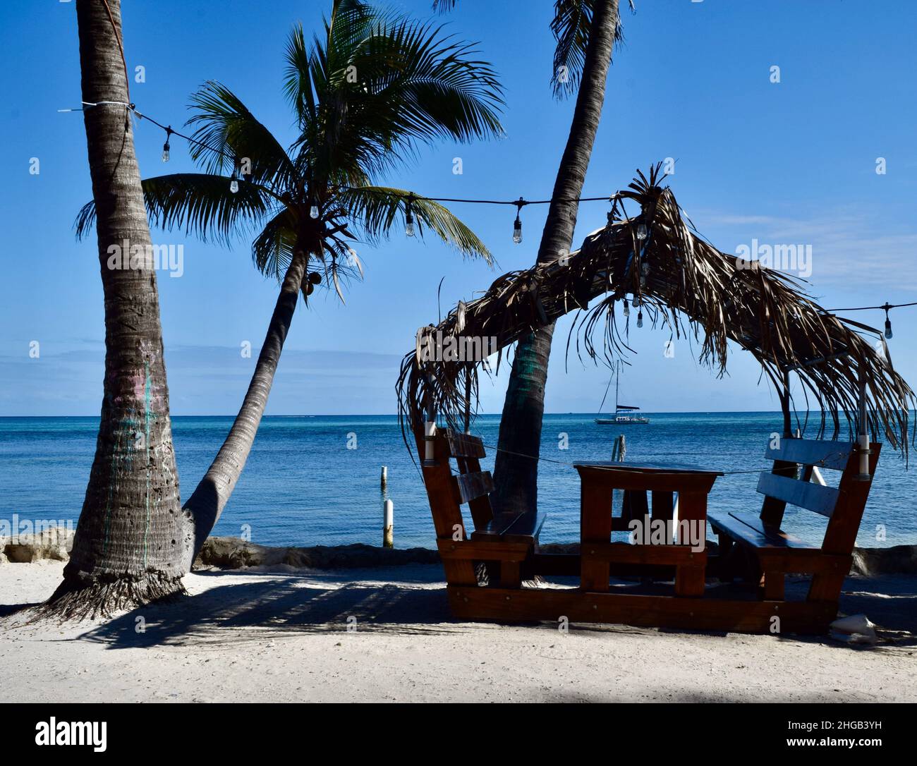 Belize Sloop A palapa-covered table and benches under the palm trees on the beach ...