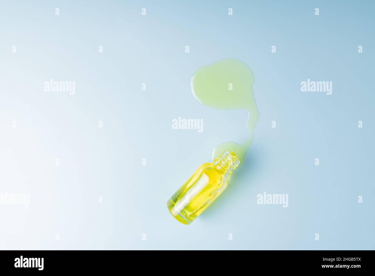 glass bottle for essential oil. Spilled serum on a blue background. Eco