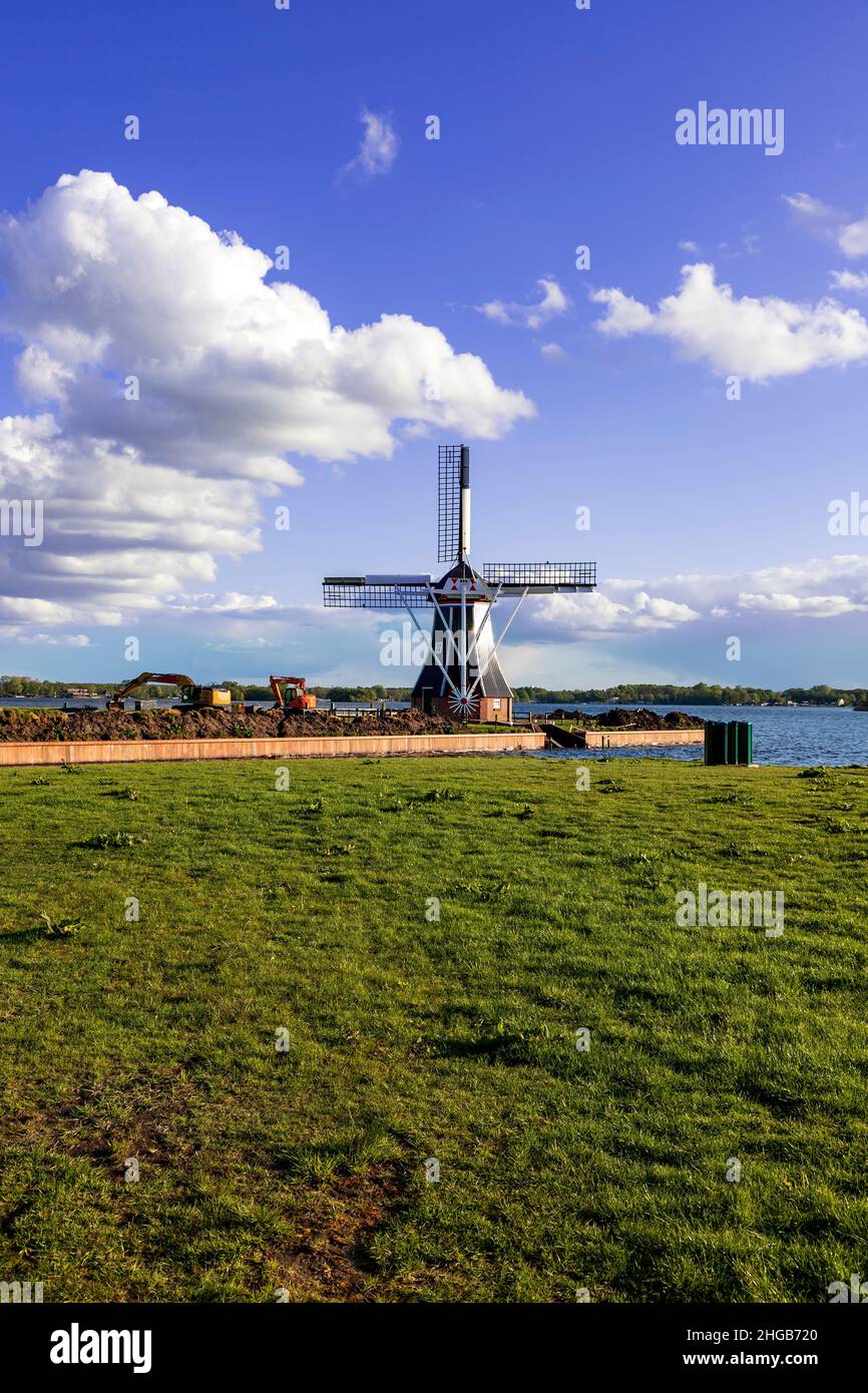 Windmill by the canal at Glimmen in Holland. Around the mills are excavators and the background is a blue sunny sky with white clouds. Stock Photo