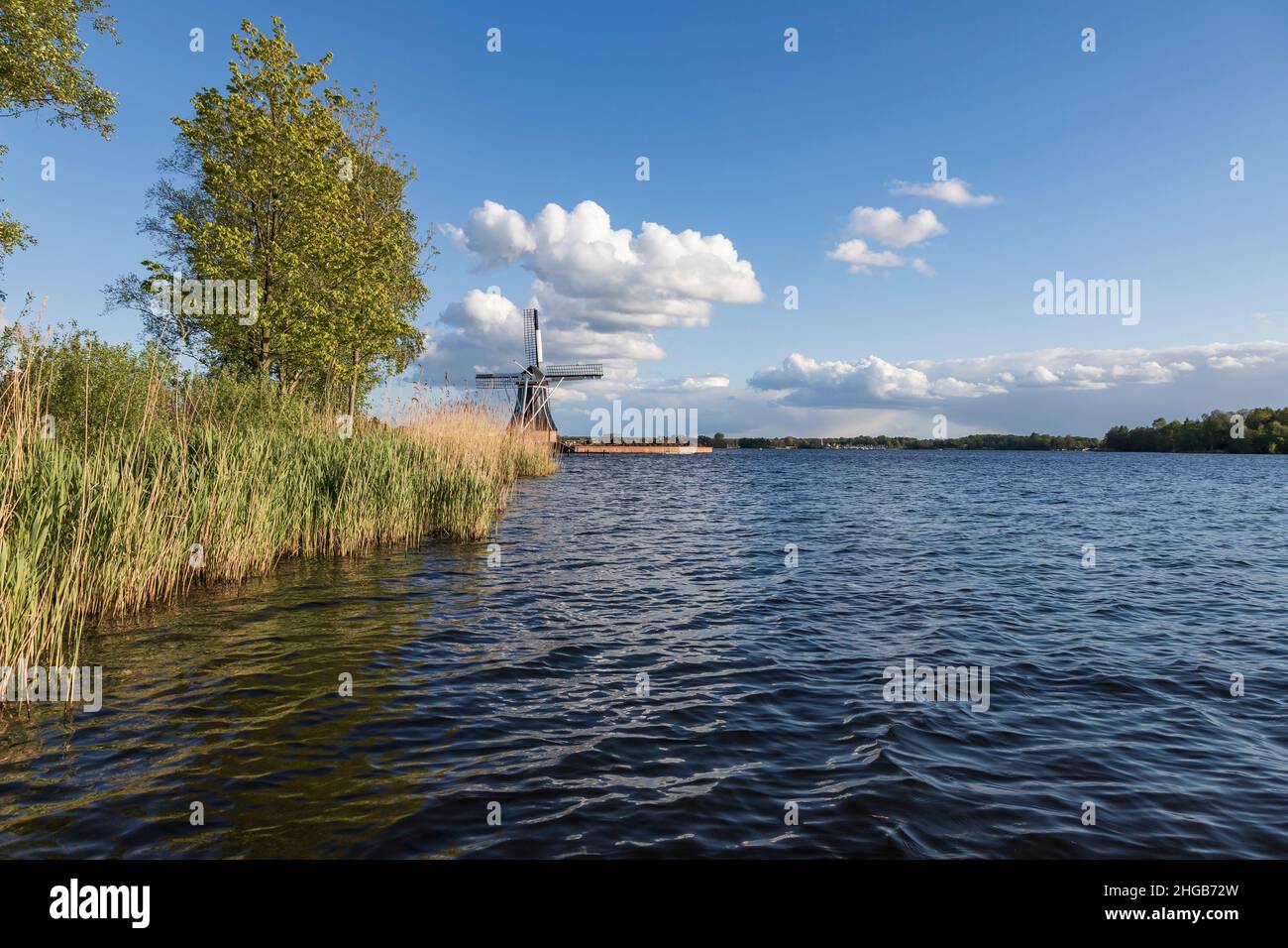 Windmill by the canal at Glimmen in Holland. The background is a blue sunny sky with white clouds. Stock Photo