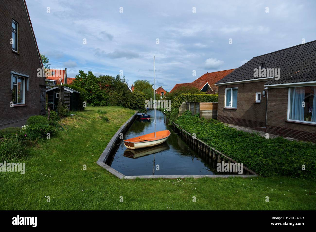 Water canal between houses in Hindeloopen in Holland. There's a boat on the water. Stock Photo