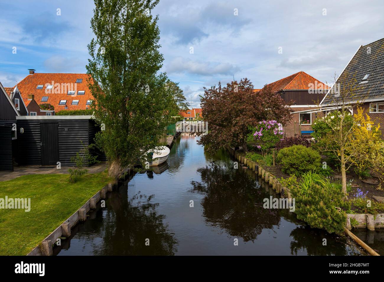 Water canal between houses in Hindeloopen in Holland. There is a boat on the water and its reflection in the water. Stock Photo