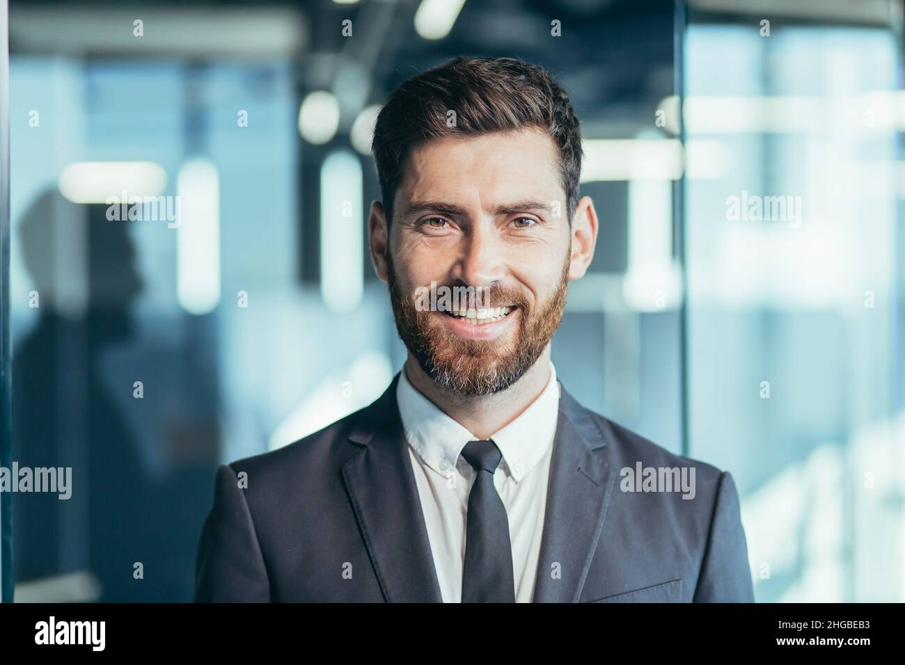 Close-up portrait of businessman with beard looking at camera and smiling, man in modern office Stock Photo