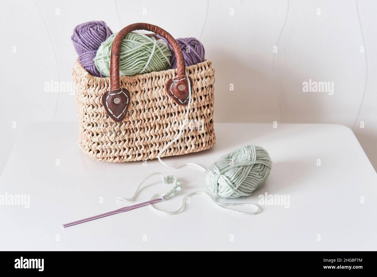 Crochet hook, chain of loops made of light green threads, straw basket