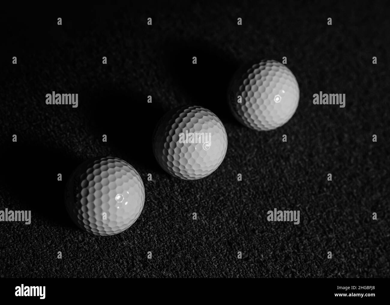Clean black and white image of three golf balls aligned in a row. Dark shadows with one side of the ball highlighted Stock Photo