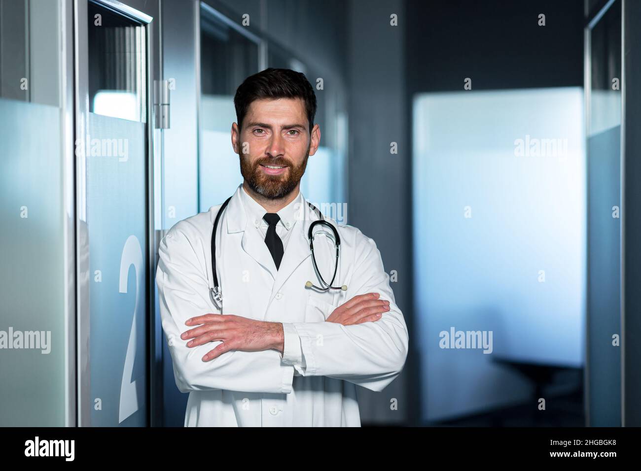 Friendly doctor smiling with crossed arms, man in medical gown, near