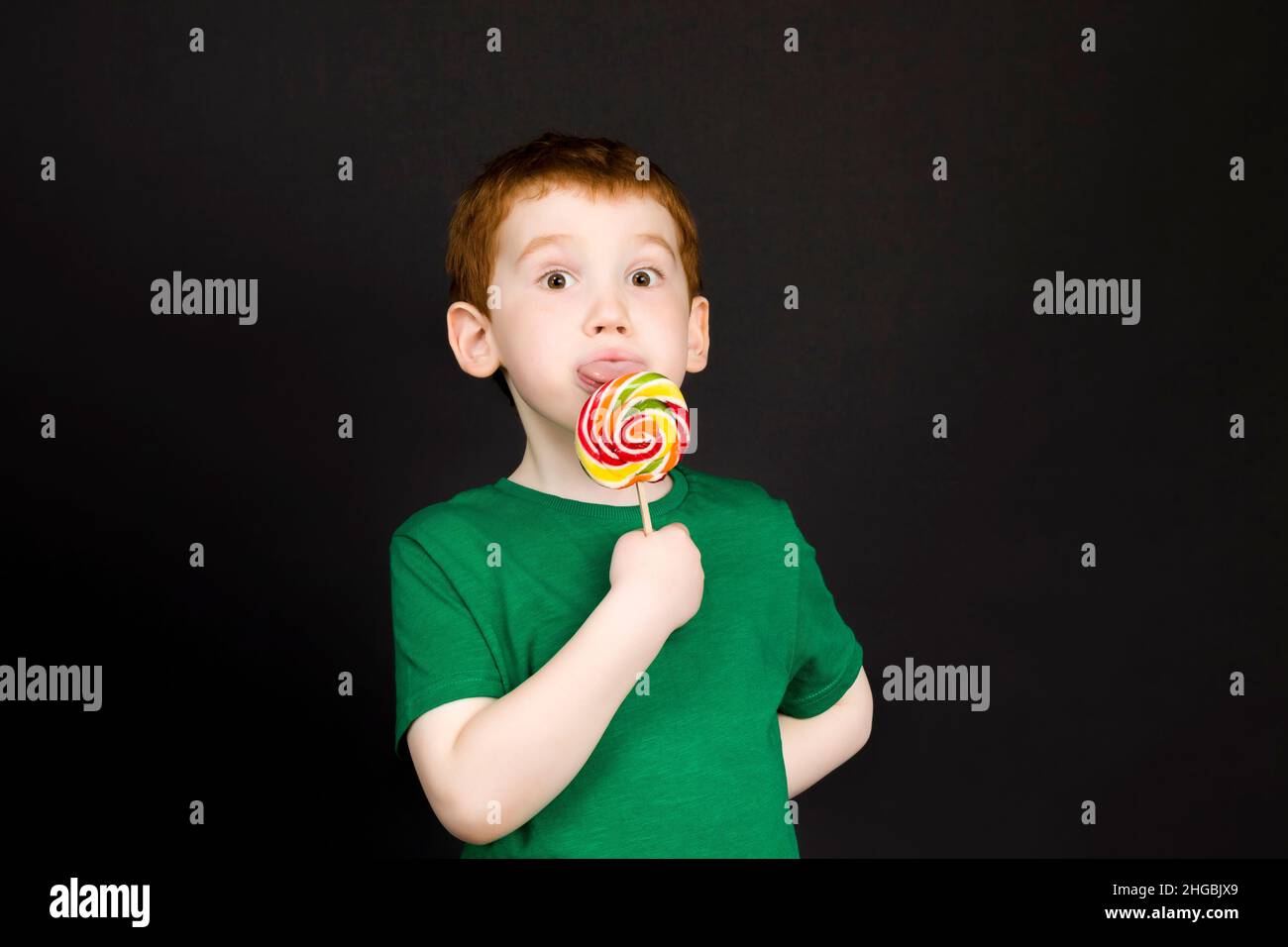 a red-haired boy with a beautiful face eats a sweet multi-colored candy ...