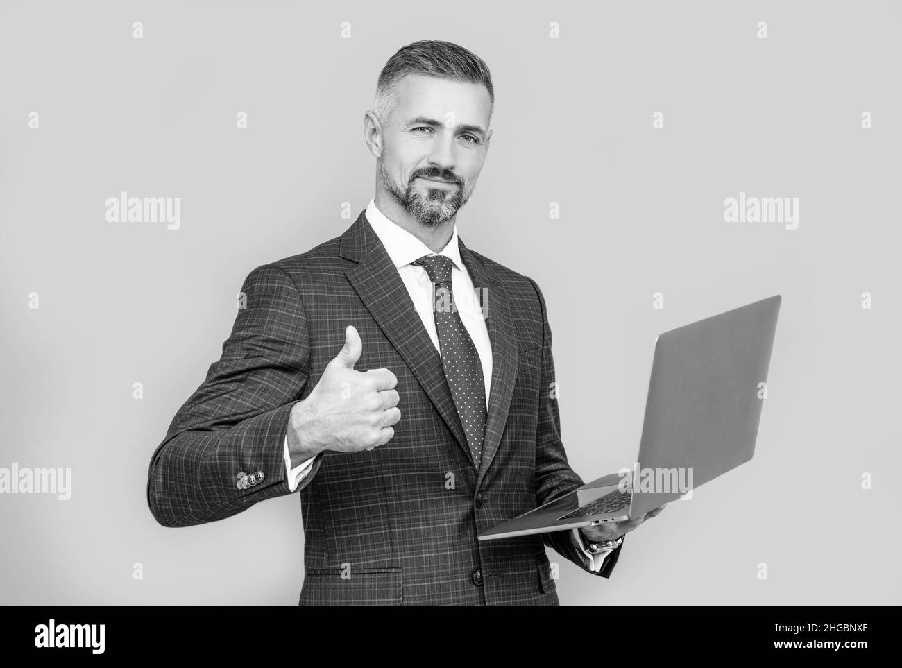confident businessman man in businesslike suit hold computer show thumb up, success Stock Photo