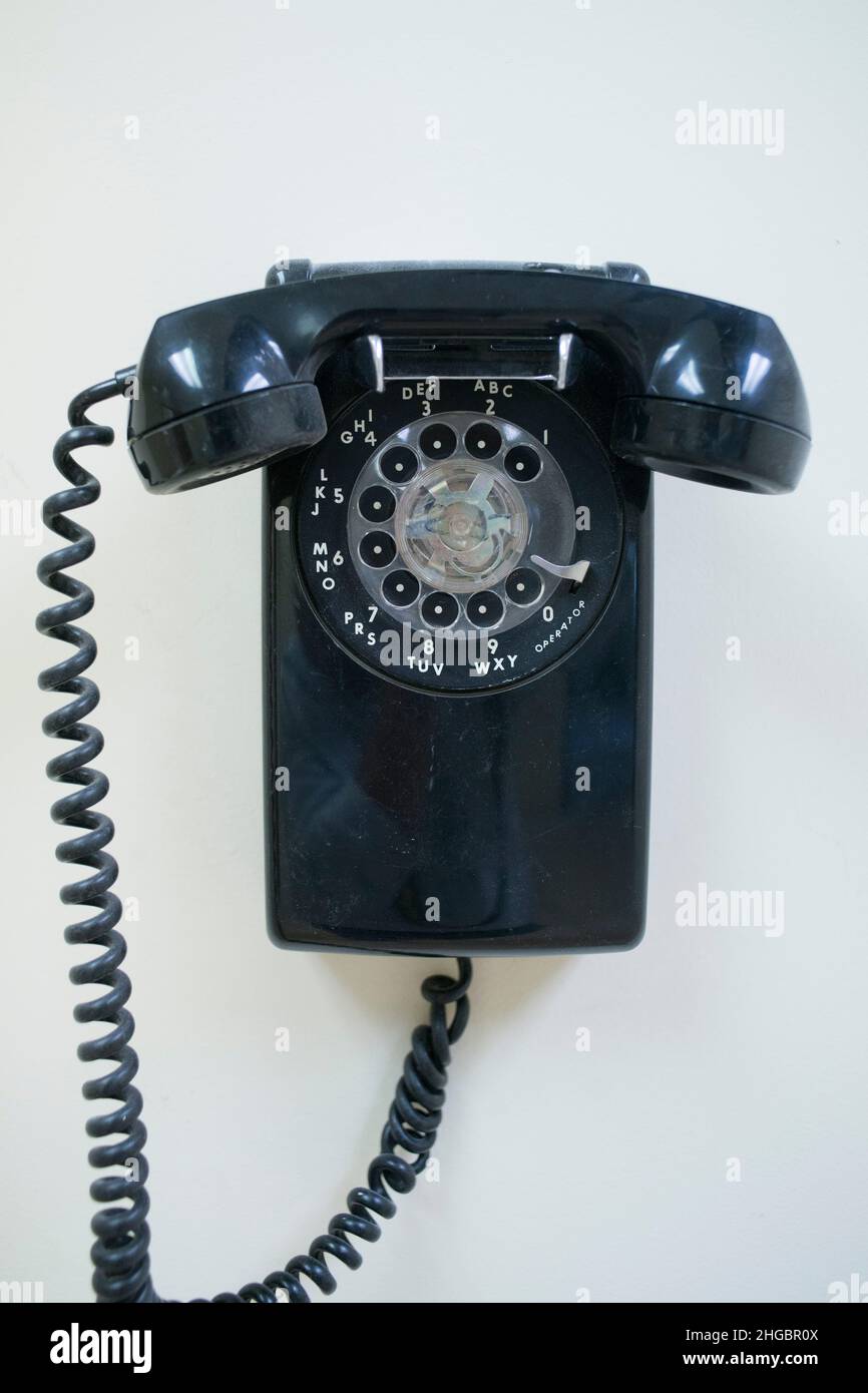 Black and dusty old rotary phone hangs on a white wall Stock Photo