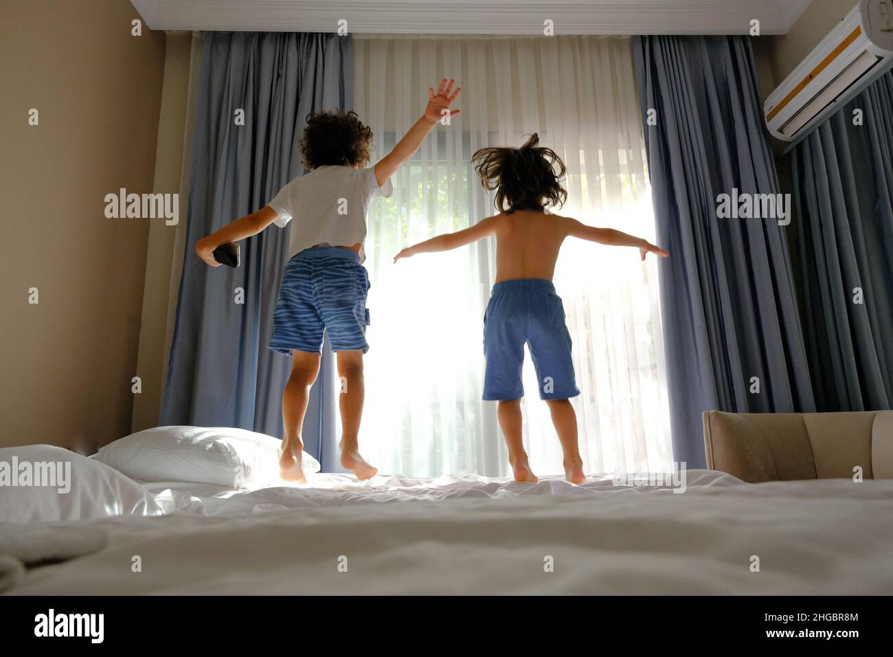 Two happy kids jumping on the bed with a phone listening to music Stock Photo