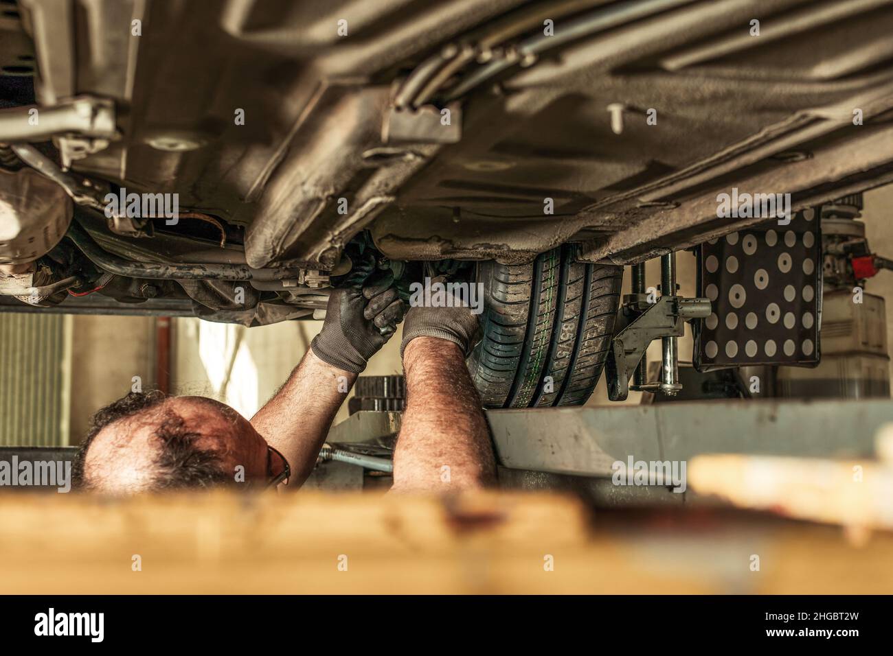 Man in a hole under a car fixing steering alignment in a garage Stock ...