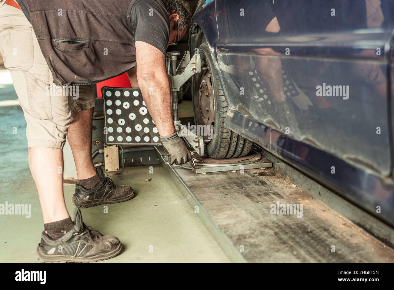 Mechanic crouched to align the steering of a car lifted by a jack in a garage Stock Photo