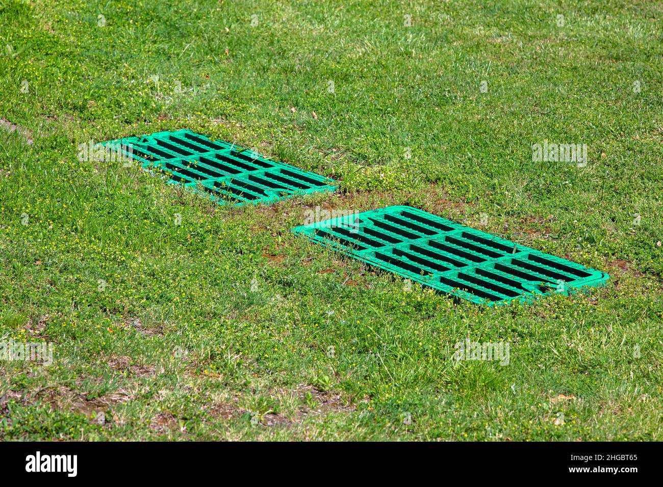 catch basin grate drainage on the lawn with green grass septic tank cover, two rectangular green eco hatches sump cesspool drainage system environment Stock Photo